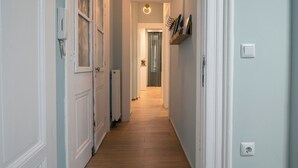 Un estrecho pasillo con piso de madera, paredes blancas y una puerta al final que da a otra habitación.