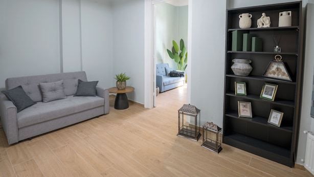 Una sala de estar moderna con un sofá gris, una mesa redonda de madera, una estantería y una planta grande.