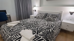 Una cama bien hecha con una colcha y almohadas estampadas con motivos de cebra, una mesita de noche con lámpara, una silla y un escritorio con computadora.