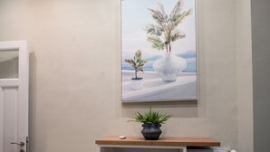 Un cuadro enmarco que muestra dos jarrones con plantas en una pared, una planta en maceta sobre un estante debajo y una puerta blanca a la izquierda.