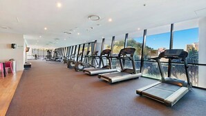A gym with treadmills aligned along a wall with large windows offering a view of the city. - Level 29 Oceanfront & City Horizon Bliss (Gold Coast)