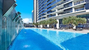 A swimming pool adjacent to a modern building with multiple balconies and a clear blue sky. - Level 29 Oceanfront & City Horizon Bliss (Gold Coast)