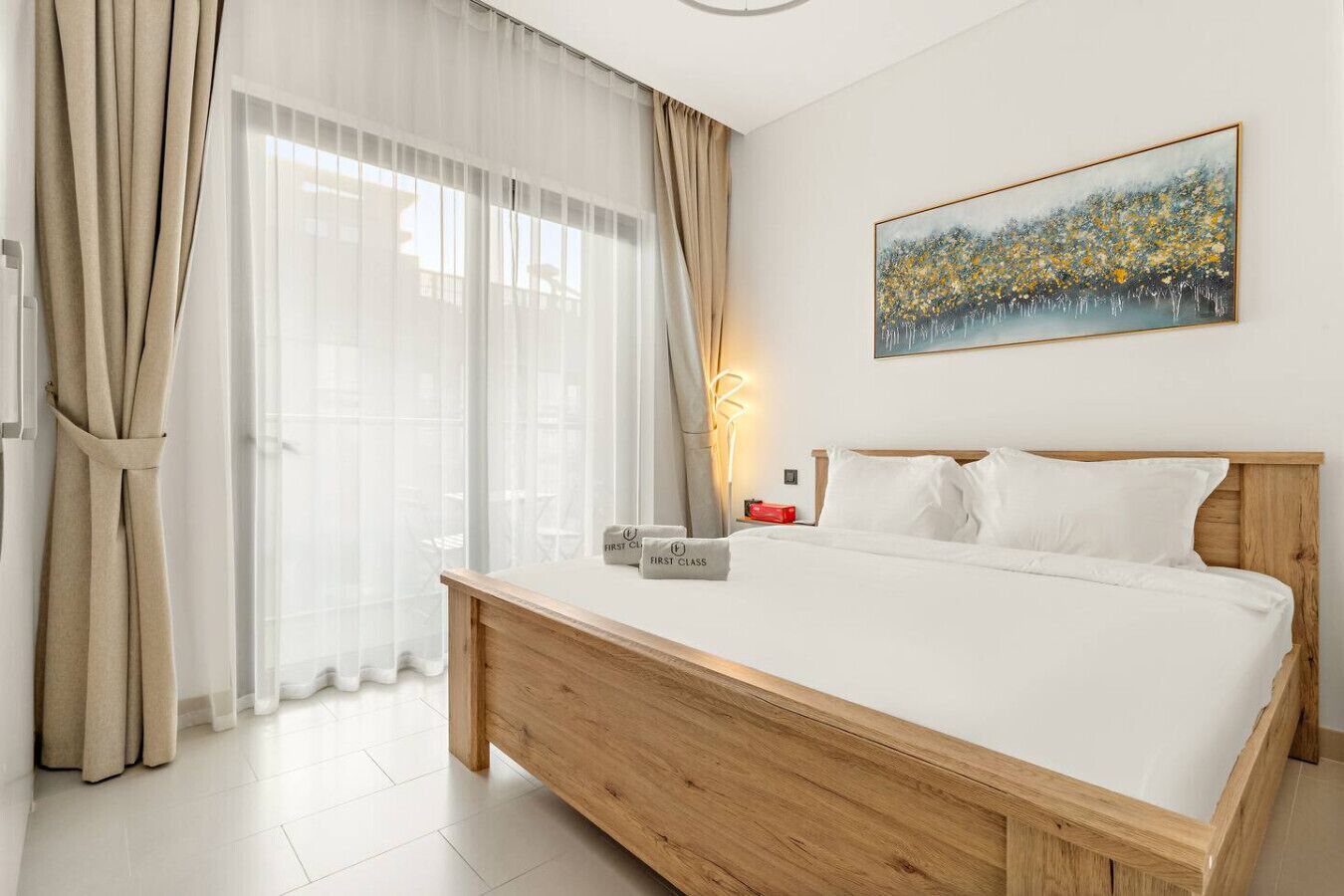Une chambre d’hôtel avec un lit en bois, du linge de lit blanc, un tableau au mur et des rideaux en voile.