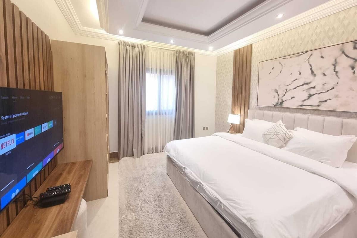 A modern hotel room with a large bed, a television on a wooden desk, and a marble accent wall.