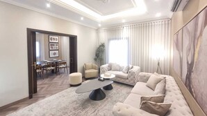 A spacious living room with a large sectional sofa, a coffee table, and a dining area with chairs and a table. - Hometel Khozama Jed (Jeddah)
