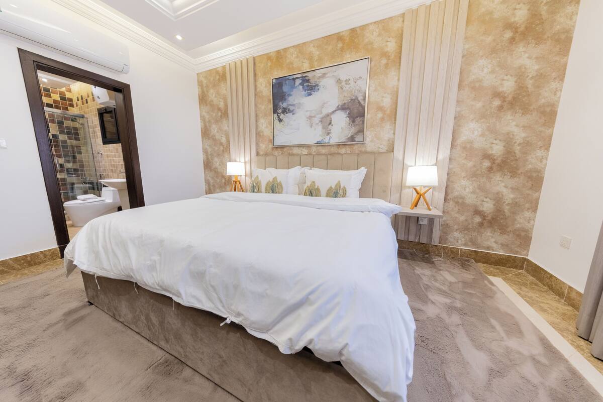 A spacious bedroom with a large bed, a modern headboard, and a large abstract painting on the wall.