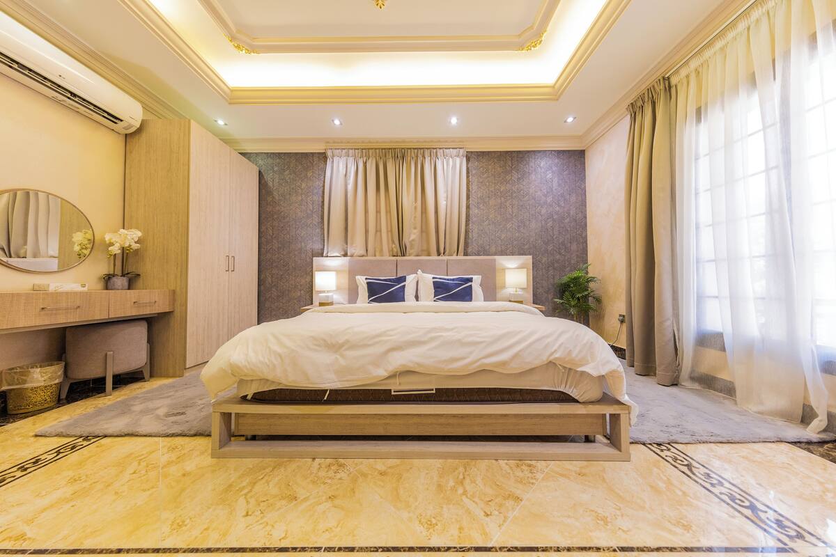A modern bedroom with a large bed, a vanity with a mirror, and a potted plant.