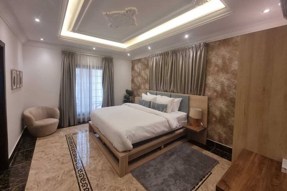 A modern bedroom with a large bed, a chair, a nightstand, and a ceiling light fixture.