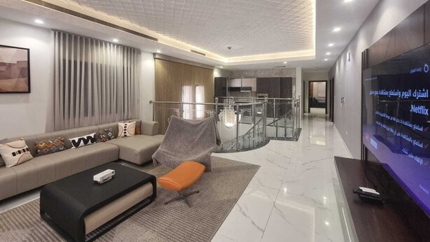 A modern living room with a sofa, ottoman, and a flat-screen TV. - Hometel Khozama Jed (Jeddah)