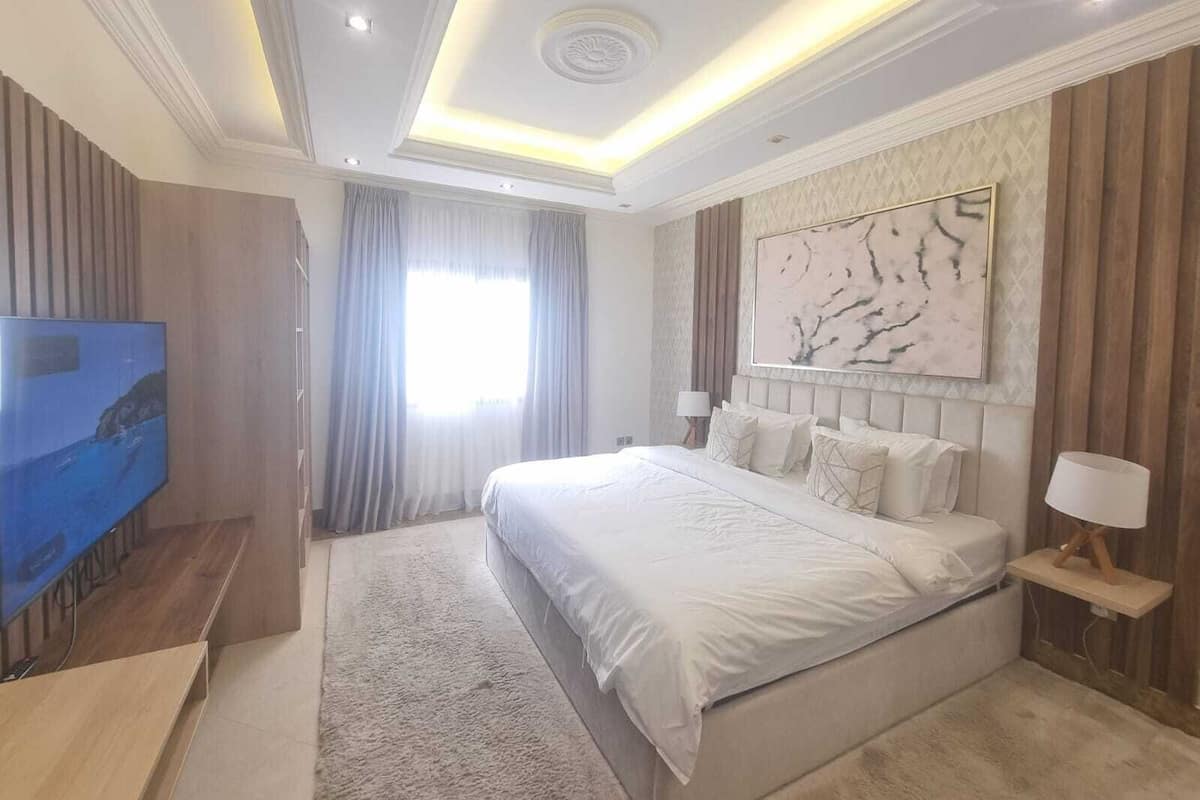 A modern bedroom with a large bed, a flat-screen TV, and a large window with curtains.