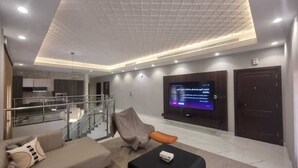 A modern living room with a flat-screen TV mounted on the wall, a sofa, a coffee table, and a staircase leading to an upper level. - Hometel Khozama Jed (Jeddah)