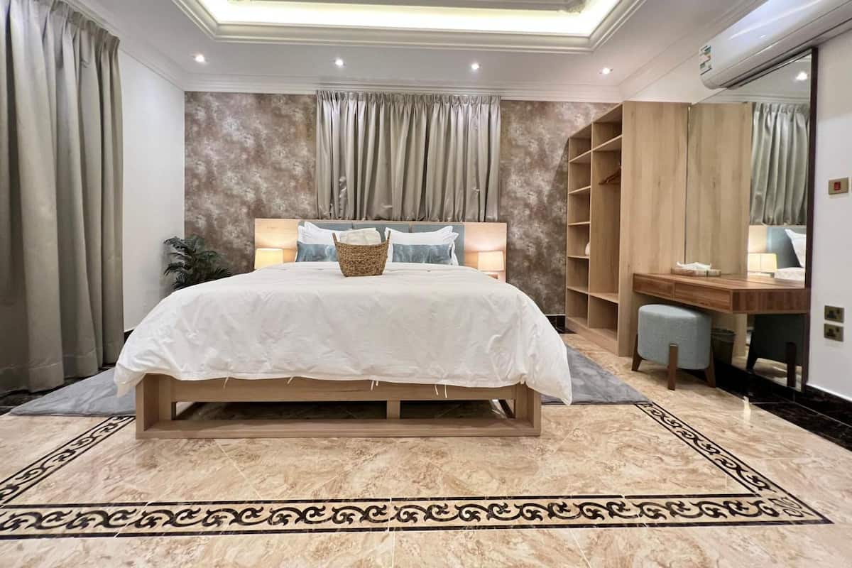 A bedroom with a large bed, a wooden desk, a chair, a wardrobe, and a mirror.