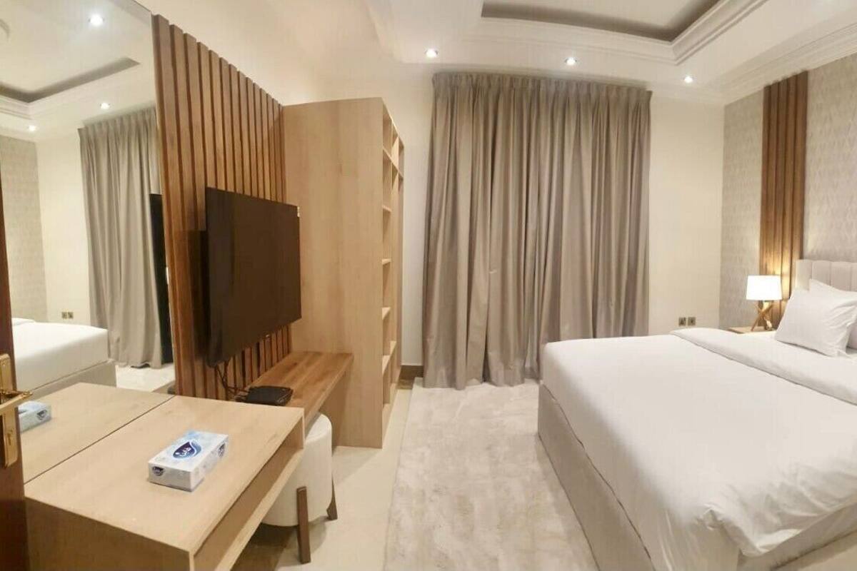A hotel room with a large bed, bedside lamps, a TV, a desk, and a wardrobe.