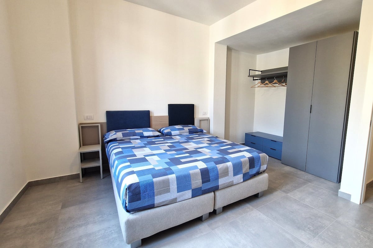 A modern bedroom with a large bed, a wardrobe, and a small desk.