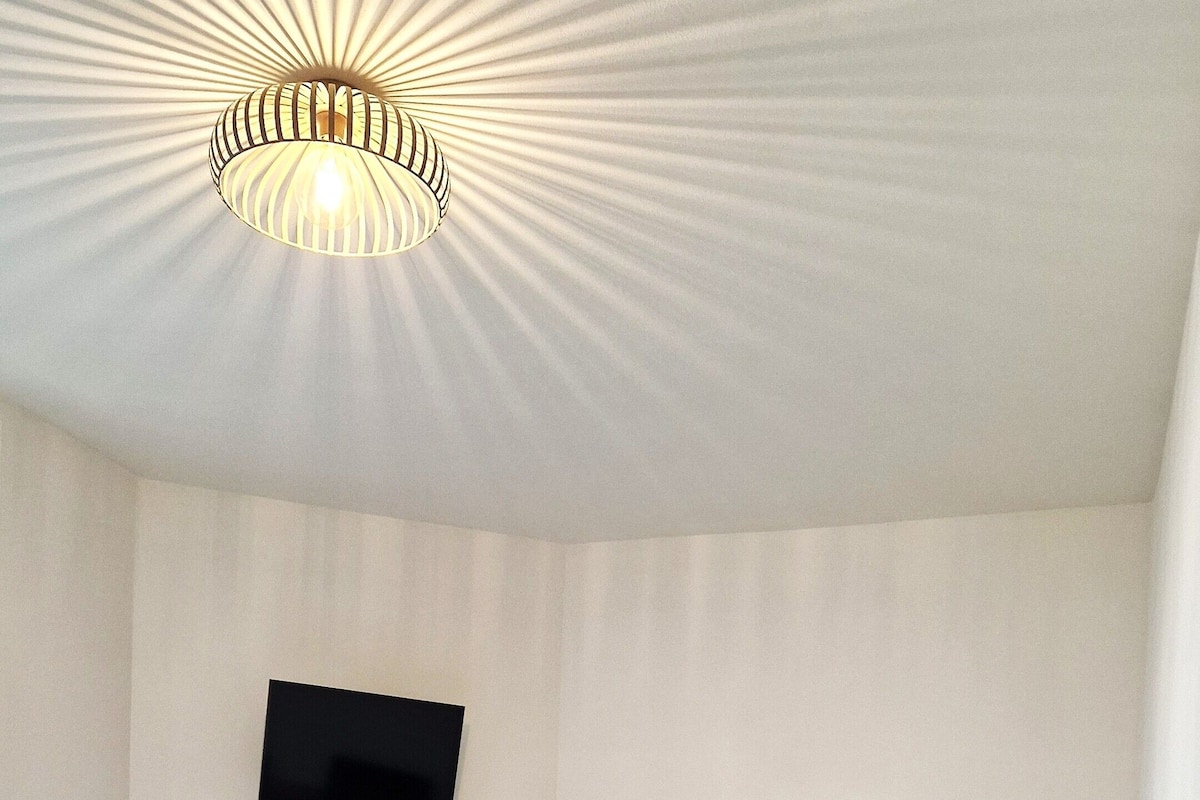 A bedroom with a bed, a round table, a TV mounted on the wall, and three mirrors.