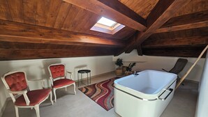 Ein gemütliches Schlafzimmer im Dachgeschoss mit Dachfenster, einer weißen Badewanne, zwei roten Polstersesseln und einem kleinen Beistelltisch.