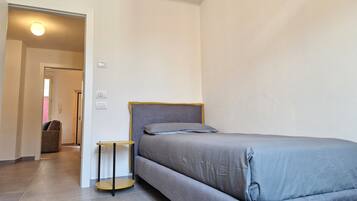 A bedroom with a bed, a bedside table, and a door leading to another room.