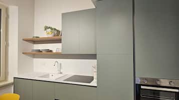 Une cuisine moderne avec des meubles gris, un évier et une cuisinière. On y trouve une chaise jaune et une fenêtre sur le côté gauche.