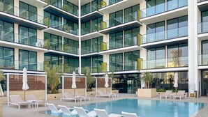 A modern hotel with a large indoor swimming pool, multiple lounge areas, and a multi-story building with large windows. - Timeless Luxury 1BR Apartment Near Dubai Marina & Iconic Palm Jumeirah (JVC)