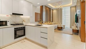 A modern kitchen with white cabinetry, a built-in oven, and a microwave. There is a dining area with a sofa and a chandelier. - Timeless Luxury 1BR Apartment Near Dubai Marina & Iconic Palm Jumeirah (JVC)