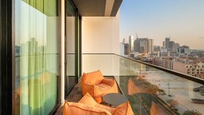A balcony with orange cushions and a small table, overlooking a cityscape with buildings and construction cranes. - Timeless Luxury 1BR Apartment Near Dubai Marina & Iconic Palm Jumeirah (JVC)