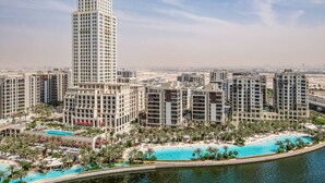A high-rise hotel with multiple floors, a pool area with palm trees, and a view of the cityscape.
