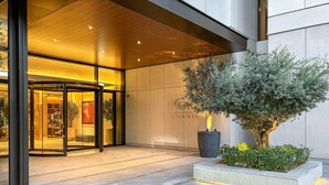 A modern hotel entrance with a glass door, a wooden ceiling, and a well-maintained garden area.