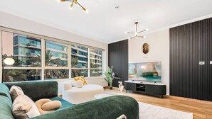 A modern living room with a green sofa, a white armchair, and a flat-screen TV.