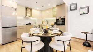 A modern kitchen with a dining area, featuring a round table with chairs, a refrigerator, and a stove.