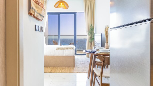 Ein modernes Hotelzimmer mit einem Bett, einem Essbereich mit Tisch und Stühlen, einem großen Fenster mit Blick und einer hängenden Leuchte.