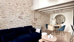 A modern living room with a stone wall, a dark blue sofa, a round dining table with chairs, and a round mirror on the wall. - Duplex 2 minutes from the arena and maison carrée (Nîmes)