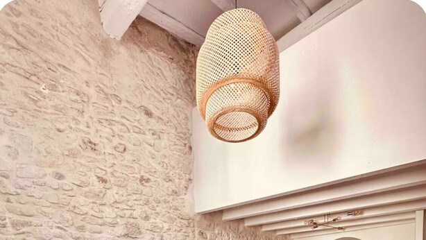 A modern living room with a stone wall, a dark blue sofa, a round wooden coffee table, and a hanging woven light fixture. - Duplex 2 minutes from the arena and maison carrée (Nîmes)