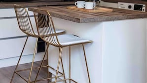 A modern kitchen with white cabinets, a wooden countertop, a gas stove, a coffee maker, and two bar stools. - Duplex 2 minutes from the arena and maison carrée (Nîmes)