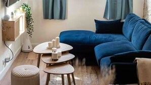 A modern living room with a blue sofa, a round coffee table, a TV mounted on the wall, and a window with curtains. - Duplex 2 minutes from the arena and maison carrée (Nîmes)