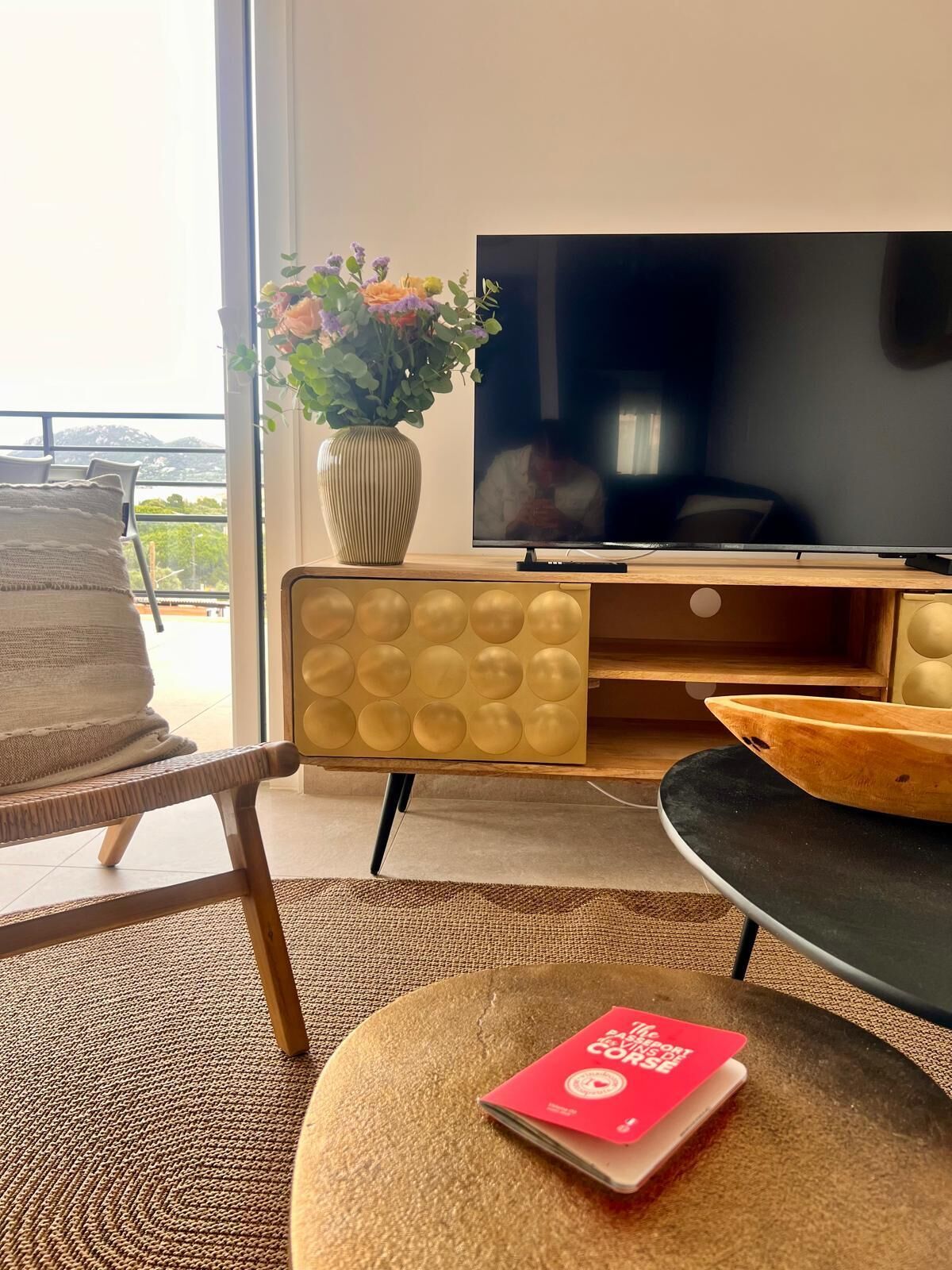 A modern living room with a sofa, a TV, a vase with flowers, and a view of the outdoors.