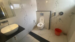 A bathroom with a white sink, a toilet, and a red bucket. - Shri Sai Palace inn (Chikkamagaluru)