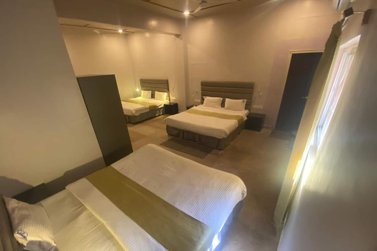 Habitación de hotel con dos camas individuales y una cama más grande, todas con ropa de cama blanca y cabeceros.