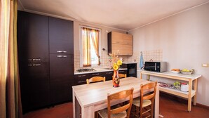 Een kleine keuken met donkere kastjes, een houten eettafel en een magnetron.