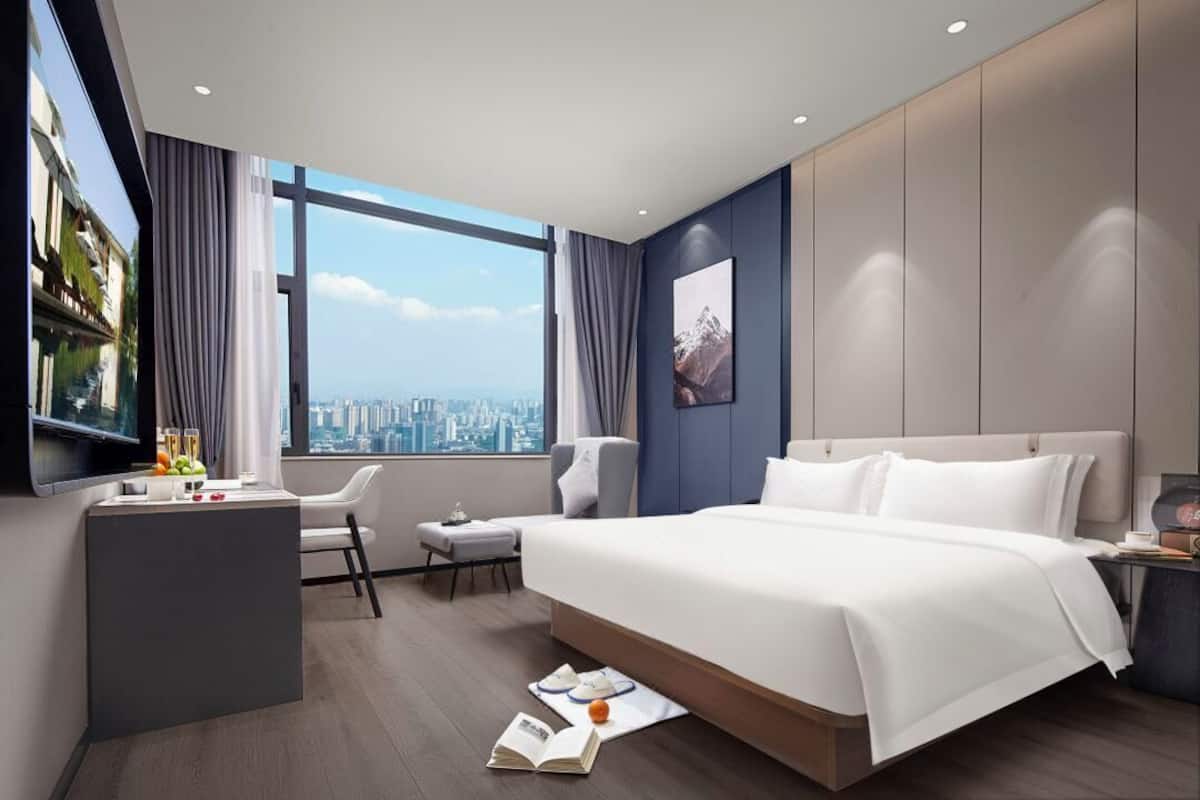 Une chambre d’hôtel moderne avec un grand lit, un bureau et une chaise. Il y a une fenêtre donnant sur la ville.