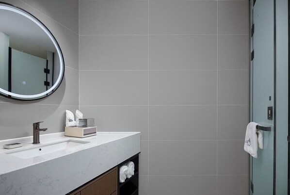 A modern bathroom with a marble sink, a round mirror, and a glass shower door. - LAN HOTEL (Chengdu)