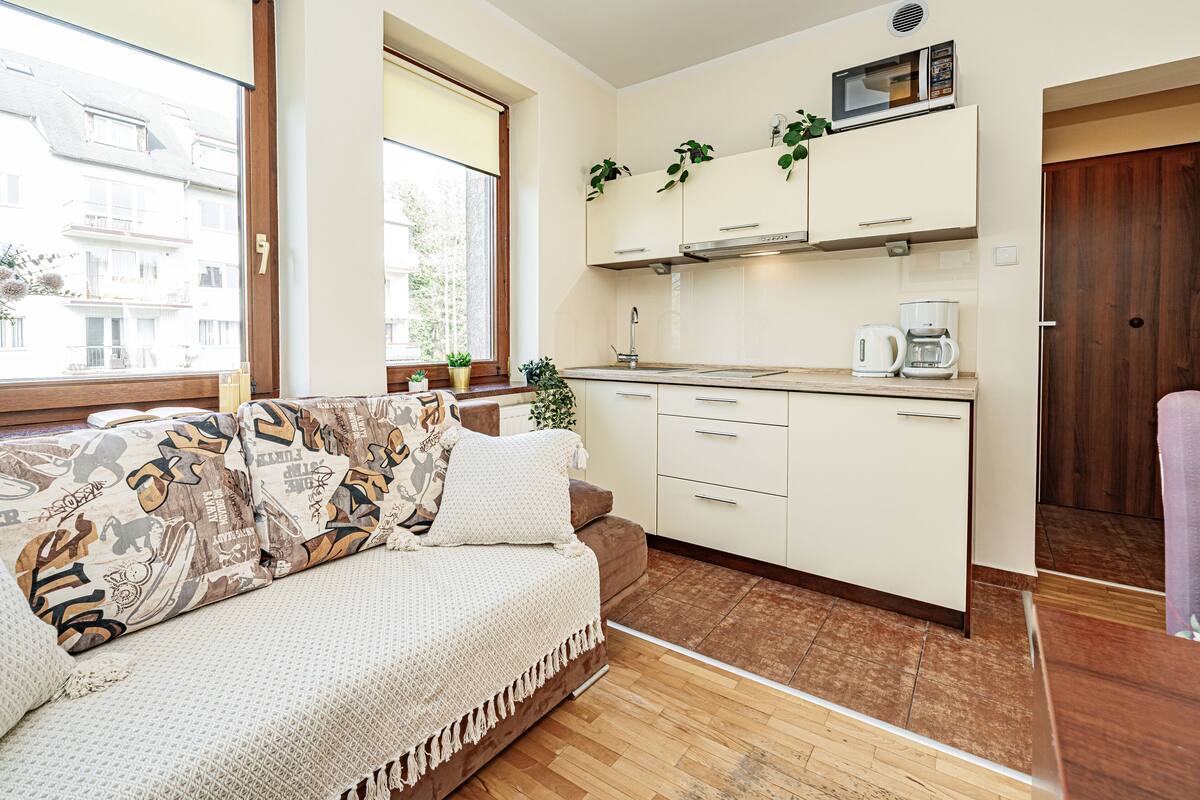 A compact living space with a sofa, kitchenette, and a view through a window.