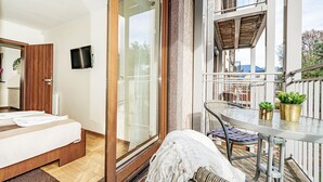 Un balcon avec une porte-fenêtre, un lit, une télévision et une petite table avec des chaises.