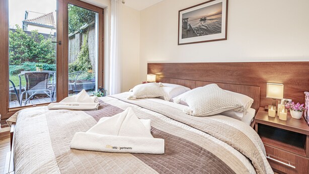 Une chambre d’hôtel avec un grand lit, deux tables de chevet avec des lampes, un tableau encadré au mur et une vue sur l’extérieur par une porte coulissante.