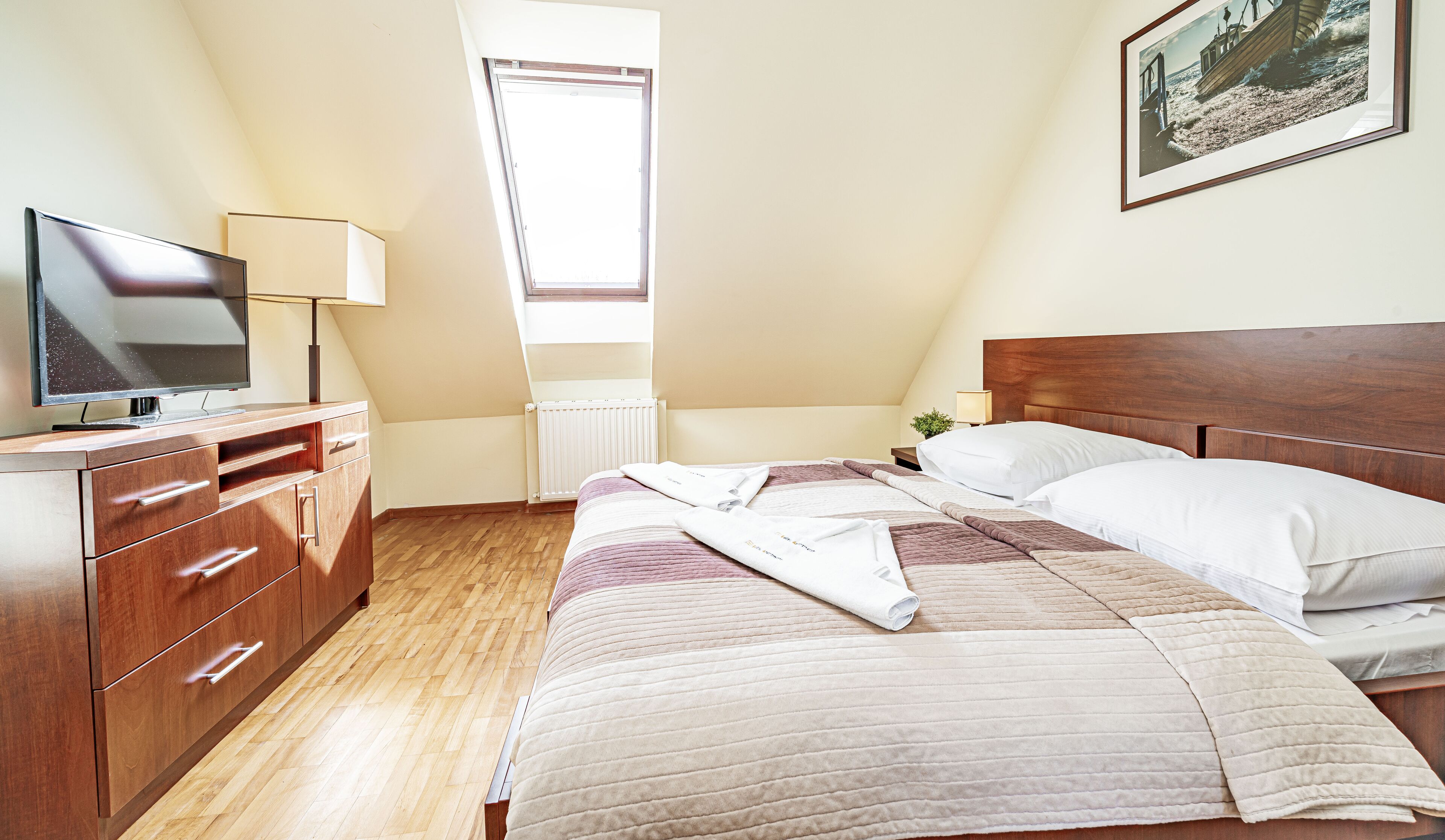 Un dormitorio con cama, televisor, cómoda y ventana.