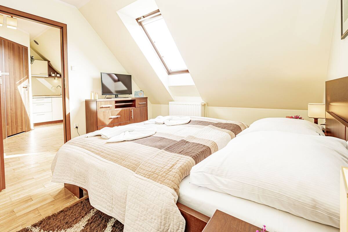 A bedroom with a bed, a TV, a desk, and a window.