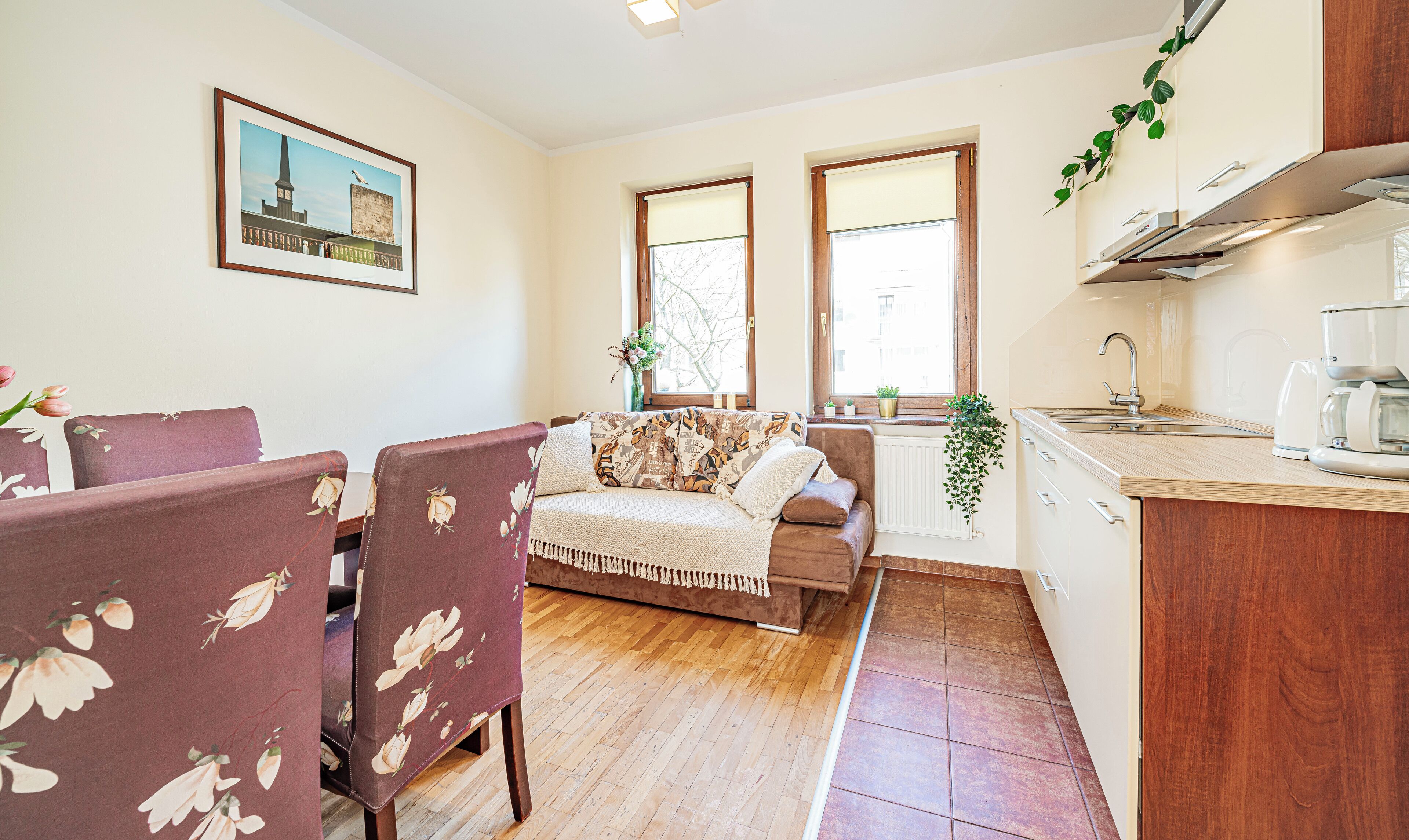 A compact living space with a sofa, chairs, a dining table, a kitchen area, and a window with a view.