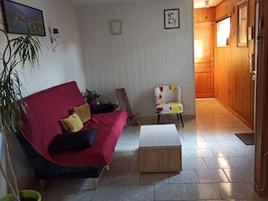 A living room with a red sofa, a wooden coffee table, a patterned armchair, and a potted plant.