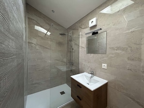 A modern bathroom with a glass shower enclosure, a wooden vanity, and a wall-mounted mirror.