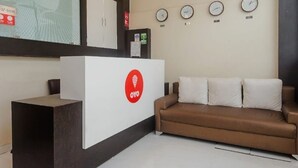 A reception area with a white reception desk, a brown sofa, and three clocks on the wall. - Hotel Venture Grand (Mumbai)
