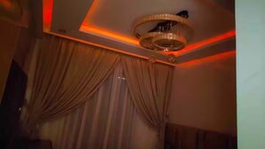 A hotel room with a bed, curtains, a ceiling light fixture, and a wall-mounted TV.
